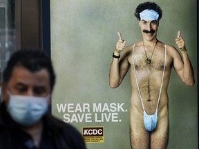 A person wearing a mask walks past a bus stop ad in New York City, Oct. 15, 2020, for the upcoming movie "Borat 2," featuring actor Sacha Baron Cohen.