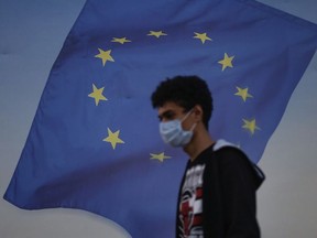 Backdropped by a poster with a European Union flag, a youth wearing a mask to help protect against the spread of coronavirus walks in Istanbul, Friday, Oct. 2, 2020.