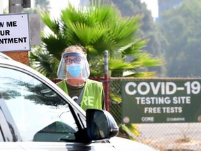 A volunteer wearing a facemask and face shield checks for COVID-19 test appointments from motorists arriving at Dodger Stadium in Los Angeles, Thursday, Oct. 8, 2020.