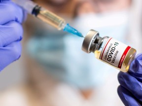 A woman holds a small bottle labeled with a "Coronavirus COVID-19 Vaccine" sticker and a medical syringe in this illustration taken on Oct. 30, 2020.
