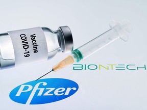 This illustration picture taken on November 23, 2020 shows a bottle reading "Vaccine Covid-19" and a syringe next to the Pfizer and Biotntech logo.