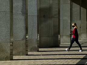 A woman wears a mask as rays of light shine through building columns on a cool sunny fall morning during the COVID-19 pandemic in Toronto on Monday, Nov. 2, 2020.