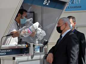 Mask-clad Israeli Prime Minister Benjamin Netanyahu is shown a demonstration of a coronavirus swab sampling at a booth during the inauguration of a COVID-19 coronavirus rapid testing centre at Ben Gurion International Airport in Lod on November 9, 2020.