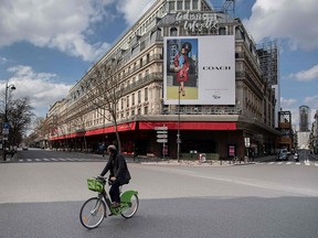 A man rides his bicycle across an empty street in front of the Galeries Lafayette shopping center in Paris, on March 18, 2020.