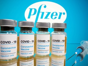 Vials with a sticker reading, "COVID-19 / Coronavirus vaccine / Injection only" and a syringe are seen in front of a Pfizer logo in this illustration taken October 31, 2020.