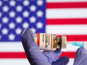 A woman holds a small bottle labeled with a "Coronavirus COVID-19 Vaccine" sticker and a medical syringe in front of displayed USA flag in this illustration taken, Oct. 30, 2020.