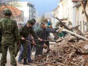 Croatian soldiers and people clean rubble next to damaged buildings in Petrinja, some 50 km from Zagreb, after the town was hit by an earthquake on Tuesday, Dec. 29, 2020.