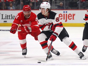 Jack Hughes of the New Jersey Devils tries to get around the stick of Luke Glendening of the Detroit Red Wings at Little Caesars Arena on February 25, 2020 in Detroit.