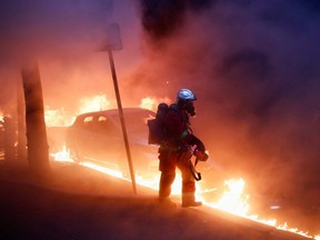A firefighter walks next to a car surrounded by flames during a protest against the "Global Security Bill" that rights groups say would make it a crime to circulate an image of a police officer's face and would infringe journalists' freedom in the country, in Paris, Saturday, Dec. 5, 2020.