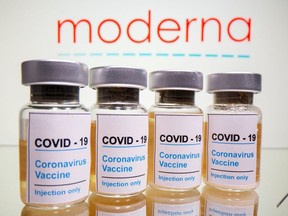 Vials with a sticker reading, "COVID-19 / Coronavirus vaccine / Injection only" and a medical syringe are seen in front of a displayed Moderna logo in this illustration taken October 31, 2020.