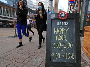 Pedestrians pass by the signs advertising happy hour outside Social Beer Haus in downtown Calgary on Tuesday, Dec. 8, 2020.