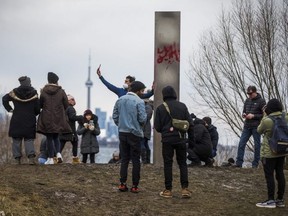 People gather around a steel monolith at Humber Bay Park East in Toronto, Ont. on Friday January 1, 2021. Installed New Years Eve, the mysterious obelisk was discovered defaced by graffiti on New Year's Day.