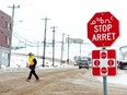 A man wearing a mask to help slow the spread of COVID-19 passes a stop sign written in English, French and Inuktitut as the territory of Nunavut enters a two week mandatory restriction period in Iqaluit, Nov. 18, 2020.