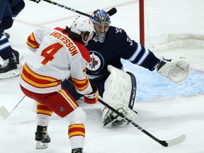 Winnipeg Jets goaltender Connor Hellebuyck is at the mercy of Calgary Flames defenceman Rasmus Andersson during NHL action in Winnipeg on Jan. 14, 2021.