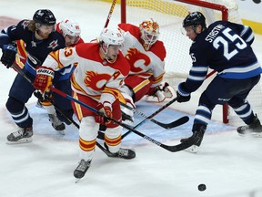 Calgary Flames centre Sean Monahan grabs a loose puck from in front of goaltender Jakob Markstrom with Kyle Connor (left) and Paul Stastny pressing during NHL action in Winnipeg on Thursday, Jan. 14, 2021.