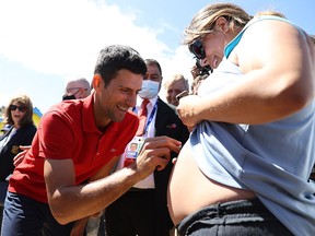 Australian Open champion Novak Djokovic signs his autograph on a pregnant woman's belly during a photo shoot at Brighton Beach Monday.