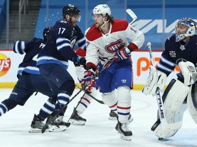 Winnipeg Jets centre Adam Lowry (left) closes on Montreal Canadiens forward Josh Anderson in front of goaltender Connor Hellebuyck in Winnipeg on Thurs., Feb. 25, 2021.