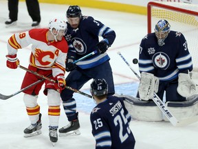 Winnipeg Jets defenceman Tucker Poolman (centre) defends as Calgary Flames forward Matt Tkachuk tips the puck past goaltender Connor Hellebuyck in Winnipeg on Thursday, Jan. 14, 2021. Poolman returns to the ice tonight when the Jets take on the Sens.