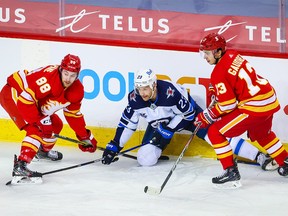 Winnipeg Jets center Trevor Lewis (23) battles for the puck with Calgary Flames left wing Andrew Mangiapane (88) and left wing Johnny Gaudreau (13) during the first period at Scotiabank Saddledome in Calgary on March 27, 2021.