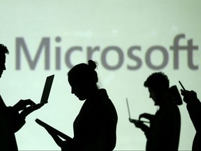 Silhouettes of laptop and mobile device users are seen next to a screen projection of Microsoft logo in this picture illustration taken March 28, 2018.