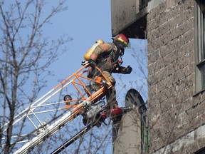 A firefighter climbs from his ladder to the 5th-floor balcony of an apartment during a five-alarm fire at a seniors' residence in Montreal, on Sunday, April 11, 2021.