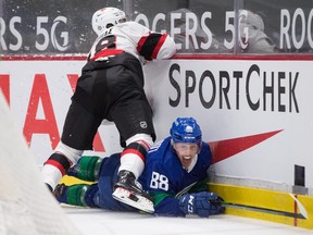 Ottawa Senators' Tim Stuetzle misses the check on Vancouver Canucks' Nate Schmidt and crashes into the boards on Thursday night.