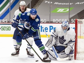 J.T. Miller of the Vancouver Canucks tries to redirect the puck on goalie Jack Campbell of the Toronto Maple Leafs while being checked by Justin Holl at Rogers Arena on April 17, 2021 in Vancouver.