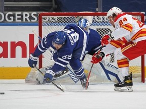 Maple Leafs forward Nick Robertson (left) clears the puck against the Calgary Flames on Tuesday night at Scotiabank Arena. Robertson was placed on the list of NHL players who are unavailable because of COVID protocol.