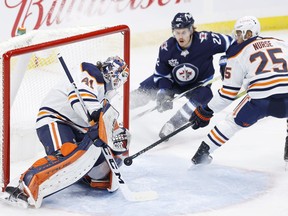 Winnipeg Jets center Mason Appleton (22) and Edmonton Oilers defenceman Darnell Nurse (25) watch as Edmonton Oilers goaltender Mike Smith (41) blocks a shot at Bell MTS Place on April 17, 2021.