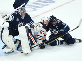 Winnipeg Jets goaltender Connor Hellebuyck (left) is bumped as Edmonton Oilers forward Connor McDavid (centre) and Jets forward Blake Wheeler fall during Game 4 of a Stanley Cup playoff series in Winnipeg on Mon., May 24, 2021. KEVIN KING/Winnipeg Sun/Postmedia Network