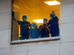 Health-care workers watch from a window at Toronto General Hospital as Toronto first responders parade down hospital row in Toronto in a salute to healthcare workers on April 19, 2020, amid the novel coronavirus pandemic.