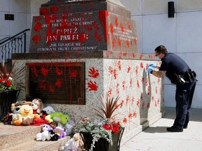 Edmonton Police Service Constable Patrick Malis collects evidence on Sunday June 27, 2021 after a statue of Roman Catholic Pope John Paul II outside the Holy Rosary Church in Edmonton was vandalized.