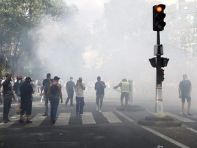 Protesters, some wearing yellow vests, stand amidst tear gas smoke during a demonstration against the compulsory vaccination for certain workers and the mandatory use of the health pass called by the French government, in Paris, Saturday, July 24, 2021.
