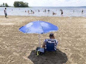 A man reads in his little spot of shade as people try to beat the heat at Cap-Saint-Jacques beach in Montreal, on Monday, June 28, 2021.