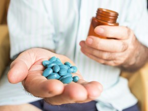 closeup of an old caucasian man with a pile of blue pills in his hand