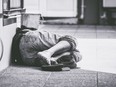 Homeless man sleep on the street, in the shadow of the building.