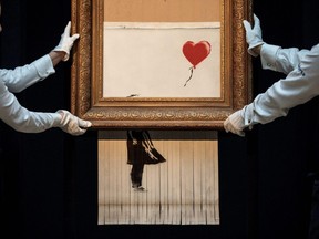 Sotheby's employees pose with 'Love is in the Bin' by British artist Banksy during a media preview at Sotheby's auction house in London, England, Oct. 12, 2018.