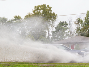 Mikkayla Longland flinches as she's sprayed by a car going through a large puddle on Sarnia Road at the base of the Brescia Hill in London. Longland was walking home from classes at Western University. Heavy rains are expected to continue to Thursday. Mike Hensen/The London Free Press