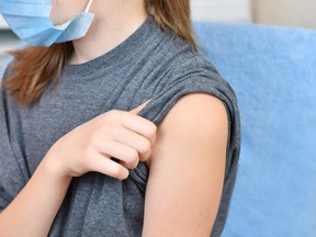 A girl wearing a blue protective mask gets ready to be vaccinated.