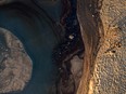 This aerial picture taken on Oct. 3, 2021 shows people overlooking oil against a berm of sand to keep it from flowing from the ocean into the Santa Ana River as an oil spill from an offshore oil rig reaches the shore and sensitive wildlife habitats in Newport Beach, Calif.