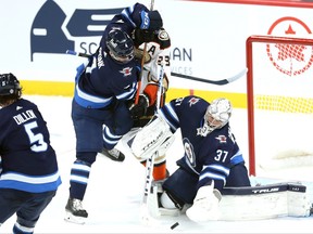 Winnipeg Jets defenceman Neal Pionk (left) ties up Anaheim Ducks forward Jakob Silfverberg while goaltender Connor Hellebuyck gloves the puck in Winnipeg on Thursday night.