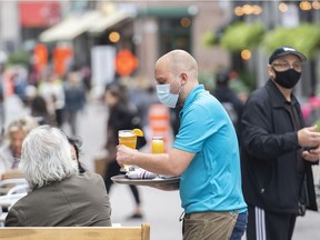 A server wears a face mask as he brings drinks to customers on an outdoor terrasse at a restaurant in Montreal on Oct. 3, 2021.