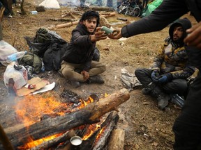 Migrants gather around a fire in a camp near Bruzgi-Kuznica checkpoint on the Belarusian-Polish border in the Grodno region, Belarus, Thursday, Nov. 18, 2021.