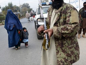 A woman wearing a burqa and a child walk past Taliban fighters along a roadside in Jalalabad on Dec. 12, 2021.