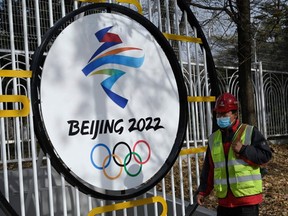 A construction worker walks past the Beijing 2022 Winter Olympic Games logo on a street in Beijing on December 11, 2021.