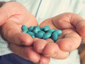 Closeup of an old man’s hands with a pile of blue pills in them.