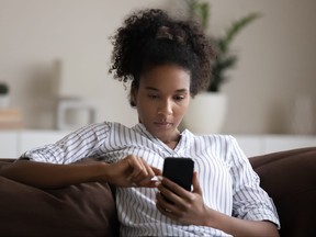 Focused African American woman using smartphone, sitting on couch