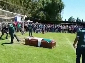 A man kicks a ball against the late player Jaime Escandar's coffin during a final send off given by his Aparicion Paine team in Paine, Chile, Sunday, Jan. 2, 2022 in this still image obtained by Reuters.