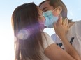 Young man and woman kissing with surgical face masks on, quarantine, Covid-19 protection. Love during coronavirus pandemic.