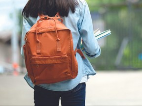 Back of university student with backpack while going to college by walking from street, teenager in campus, education concept
